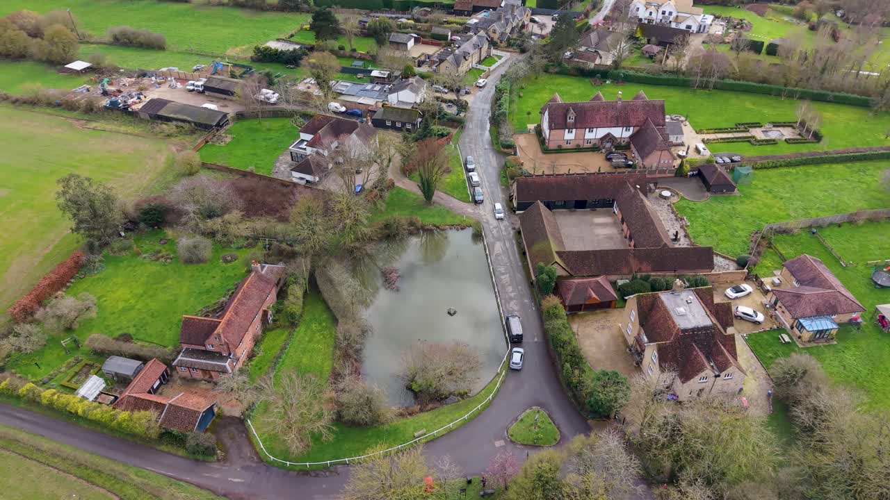 Chapmore End drone shot rises backward over the main road, duck pond and village houses in rural Hertfordshire, England, revealing countryside streetscape and calm suburban life