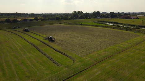 tractor makes rows of grass to pack them into silo bales, aerial orbit sunset