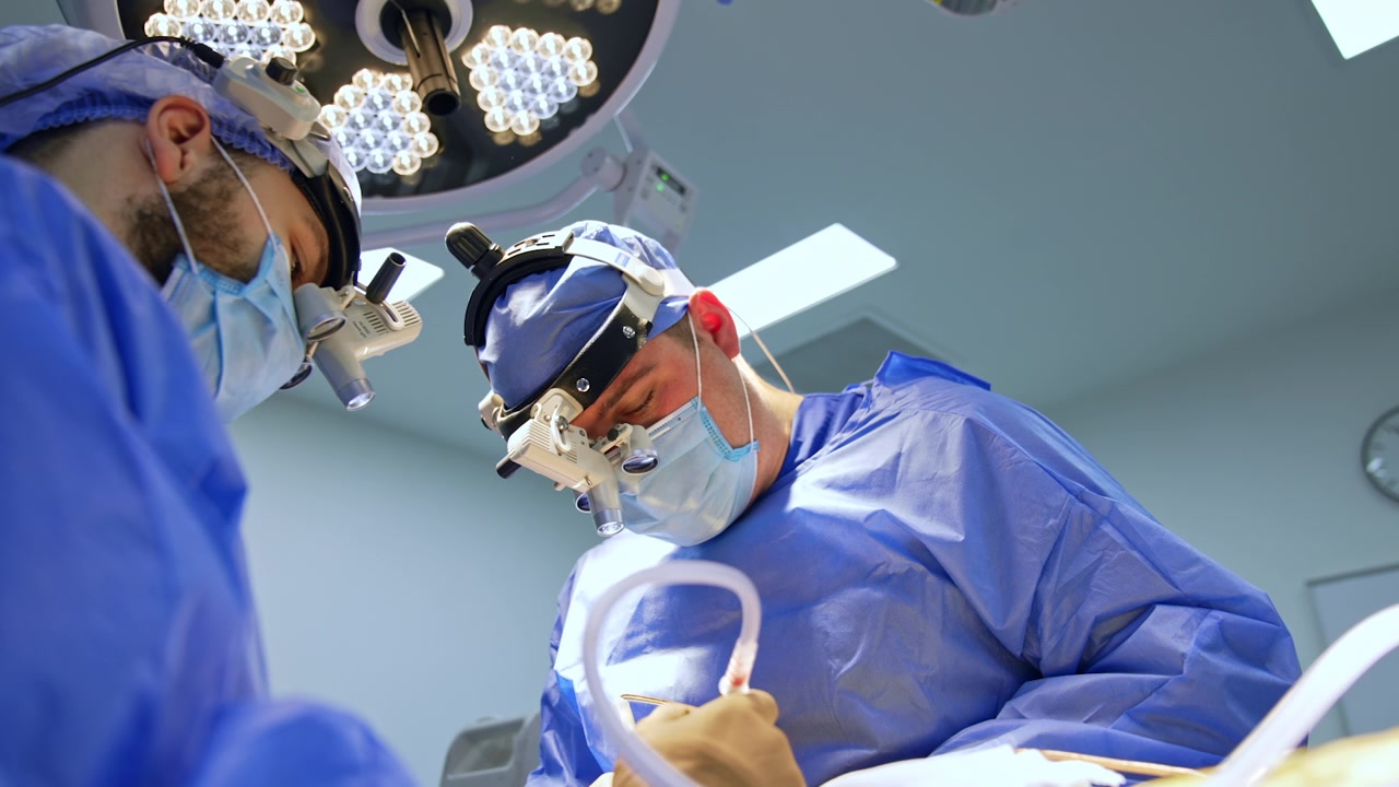 Kyiv, Ukraine, 5 May 2026: Two neurosurgeons with loupe headsets working under surgical lights from below angle.