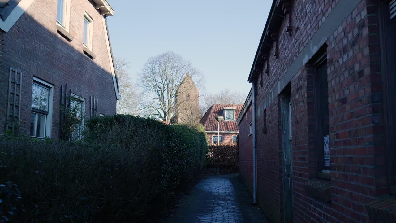 Schmale Backsteingasse zwischen Häusern, die zu einem entfernten Kirchturm führt