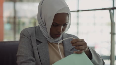 mujer negra con hijab mira dentro de la bolsa de compras en el centro comercial