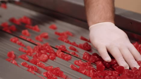mano enguantada haciendo control de calidad de vitaminas gomosas rojas en fábrica