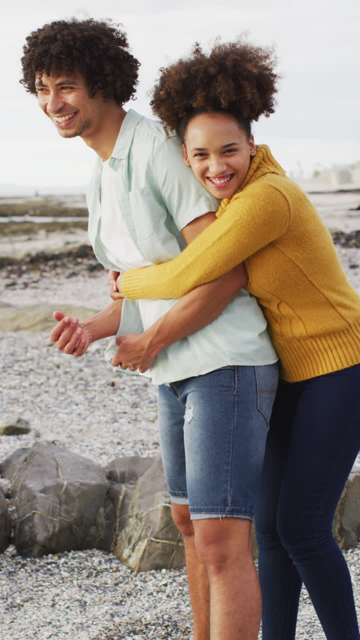 video vertical de una feliz pareja biracial abrazándose en la orilla del mar