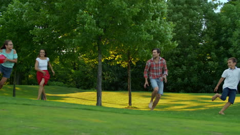 Familia-Corriendo-En-Campo-Verde.-Padres-Y-Niños-Jugando-Con-Pelota-Al-Aire-Libre