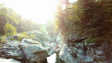 Wilder-Gebirgsfluss-Im-Sonnenlicht-Mit-Schöner-Alter-Brücke-Im-Hintergrund-Luftaufnahme-Des-Frischen-Gebirgsflusses-In-Der-Schweiz