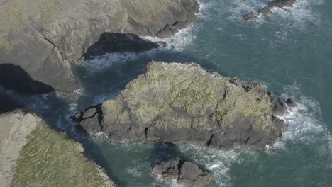 las olas del océano chocan contra y las aves aterrizan en el islote de la costa rocosa escarpada