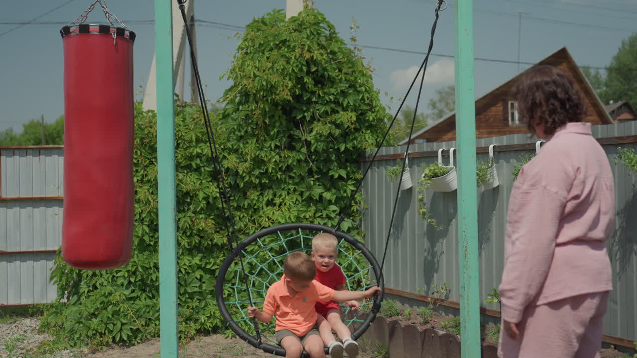 Children Play Outdoors, Sunny Yard With Children And Swing, Woman Teaches Kids On Sunny Backyard Swing, Woman Guides Children On Sunny Backyard Swing Amid Playful Summer Surroundings