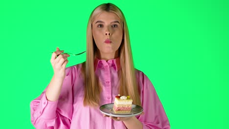 pretty blonde woman eating delicious cake, studio portrait with green background