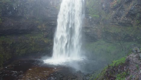 toma aérea de un dron de una espectacular cascada con una cueva detrás y troncos de árboles cortados 4k