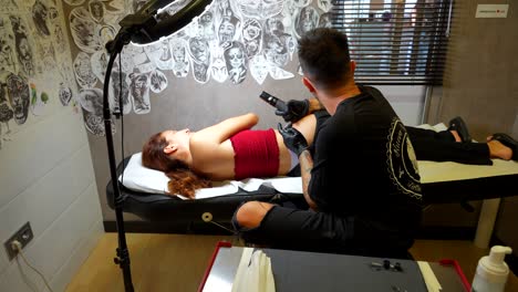 redheaded woman lies on a stretcher for tattoo session inside a studio