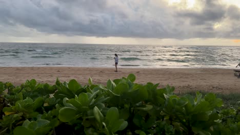 woman looking out at ocean turns around from far away to take picture