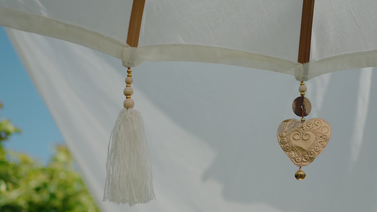 Brass heart and tassel hanging from white sunshade, symbolizing elegance and love