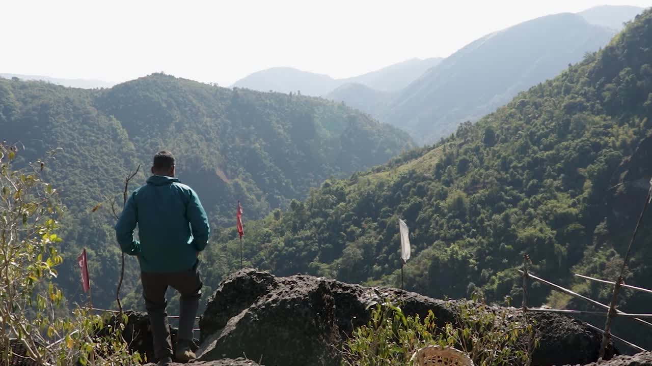 mawryngkhang trek meghalaya india에서 평평한 각도의 비디오에서 아침에 녹색 숲과 안개 낀 푸른 하늘이 있는 산 정상에 있는 고립된 청년