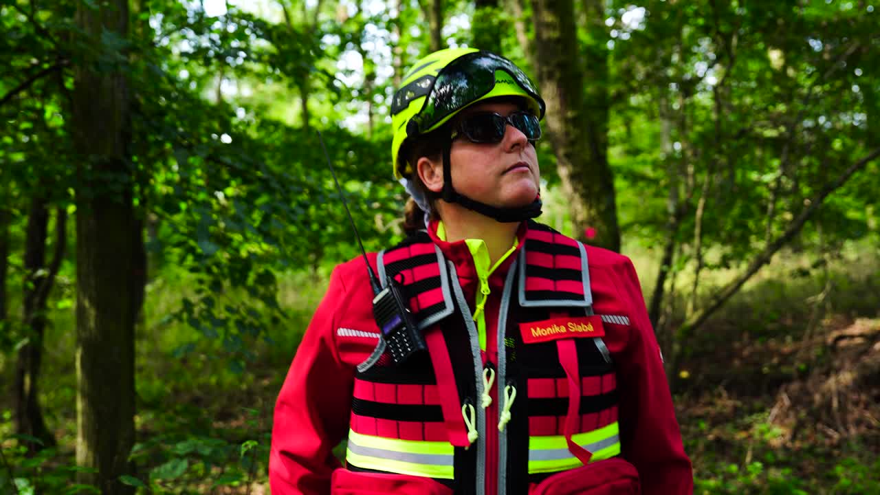 Woman in red uniform, green helmet and dark sunglasses while in forest, Czechia