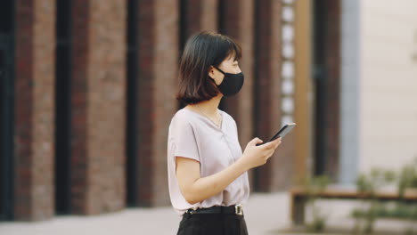 Asiatische-Frau-In-Maske-Benutzt-Telefon-Auf-Der-Straße