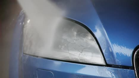 detail of the headlight and grill from a blue audi tt being washed with high pressure water