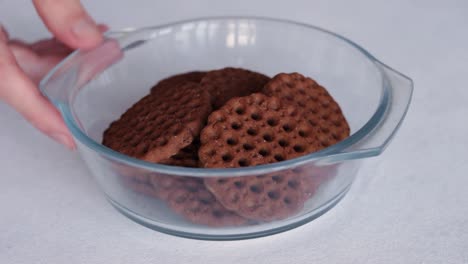 la mano pone un tazón de vidrio de galletas de chocolate sobre la mesa y luego se lo quita de nuevo