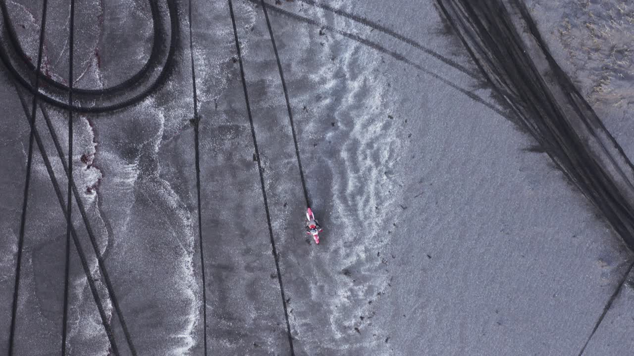 검은 모래 해변에서 운전하는 모터크로스 자전거, 위에서 아래로