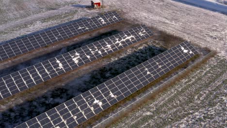 vista aérea de drones de una estación de paneles solares ligeramente cubierta de nieve que alimenta una granja