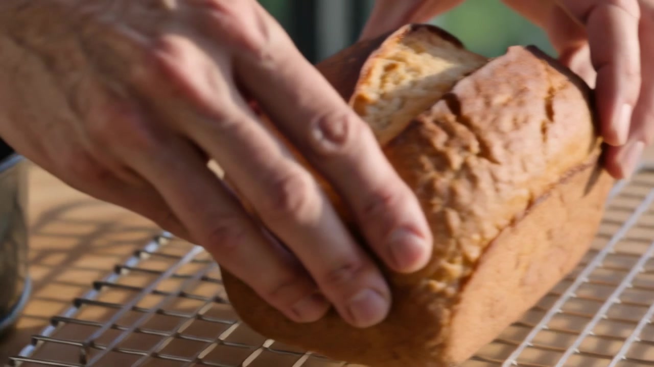 Reaching hands gripping loaf, sliding from springform pan onto wire rack in kitchen to cool