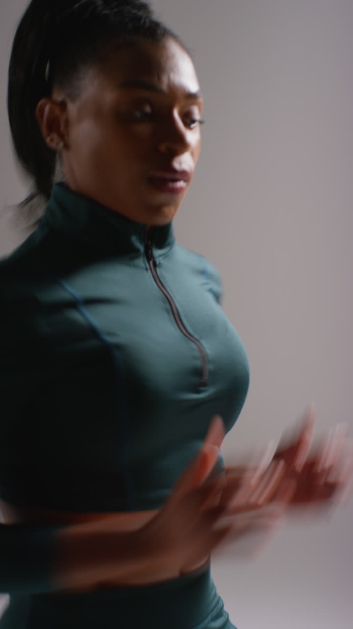 video vertical de primer plano de estudio de una atleta que lleva un traje de entrenamiento corriendo en el lugar y recuperándose después del ejercicio