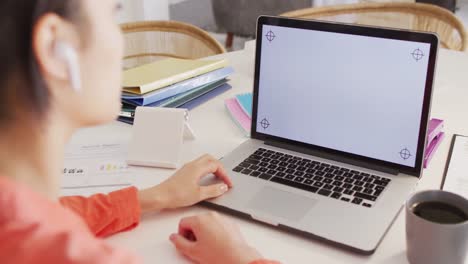 biracial woman sitting at table and working with laptop with copy space