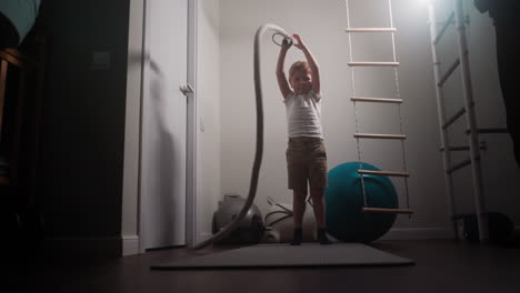 Blond-boy-waves-battle-rope-standing-near-gym-equipment