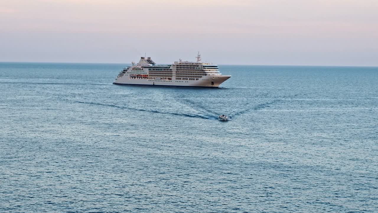 Cinematic shot of a touristic ship in the sea near the coastline at sunset