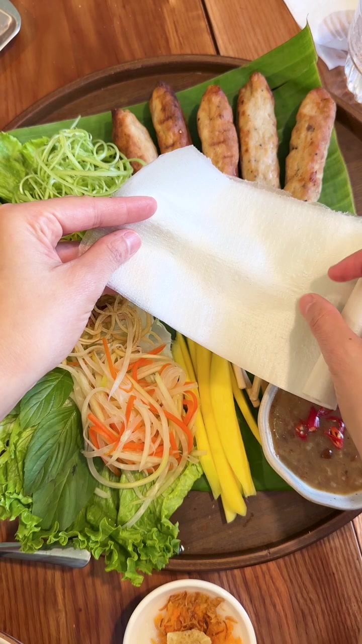 Tampilan atas tangan membentangkan kertas nasi di atas piring berisi babi panggang dan sayuran