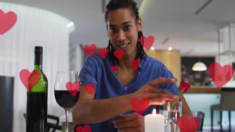 Animación-De-Corazones-Sobre-Un-Hombre-Birracial-Bebiendo-Vino-Y-Haciendo-Videollamadas