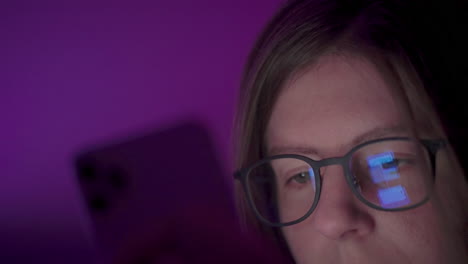 reflection of phone screen on girl's glasses as she browses social media on smart phone late at night