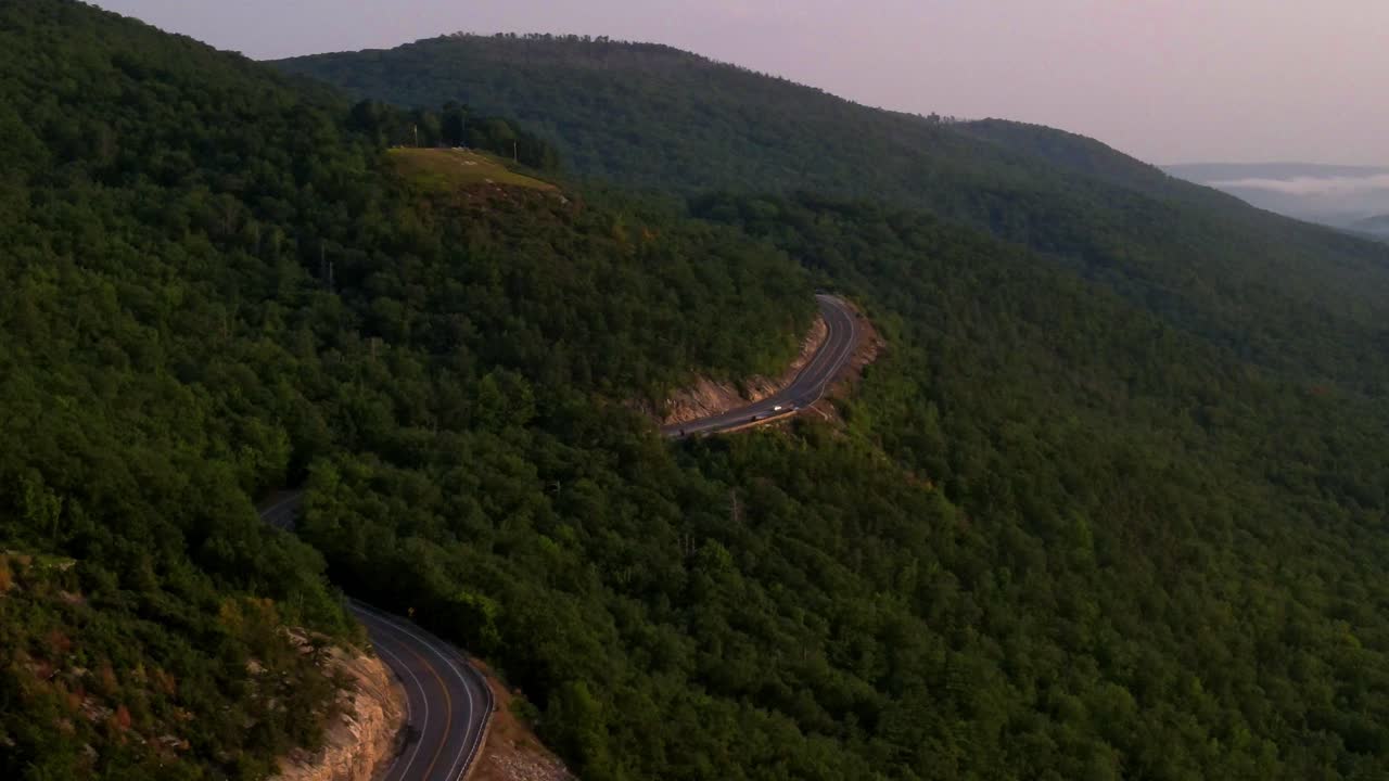 Aerial drone footage of winding scenic road in Appalachian mountains during beautiful summer sunset with golden light. This is in the Shawangunk Mountain sub-range, located in New York's Hudson Valley