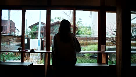woman looking out a window at a japanese cafe on a rainy day