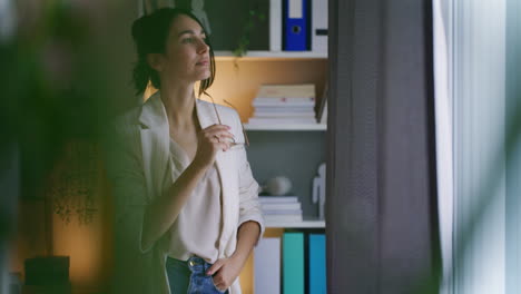 Happy-Pensive-Woman-Stands-by-Window-in-Office