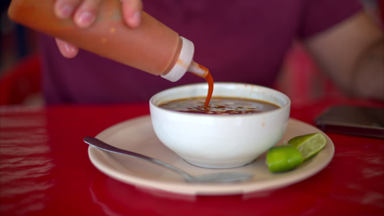 Slow motion close up of a latin man adding red hot chilli sauce to his barbacoa broth in a restaurant in Mexico