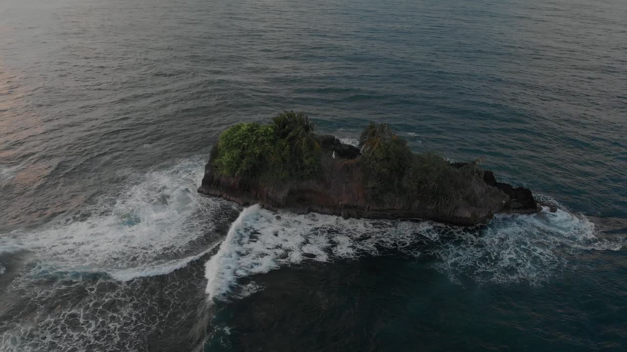 Small Tropical Island In The Middle Of The Blue Ocean With Sea Waves Crashing On The Cliff During Sunset.-  aerial shot