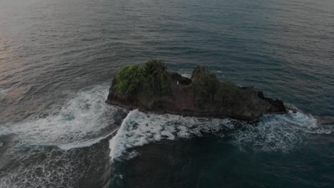 small tropical island in the middle of the blue ocean with sea waves crashing on the cliff during sunset.-  aerial shot