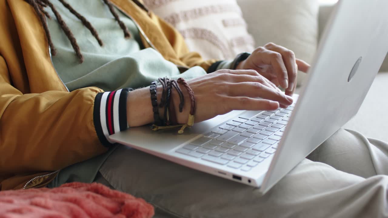 Uomo di mezza età che apre un laptop color argento e scrive da remoto sul divano in soggiorno