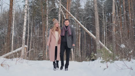 In-the-winter-snowy-forest,-young-men-and-women-dressed-in-coats-and-scarves-are-walking-and-having-fun.-Loving-couple-spend-together-valentines-day.