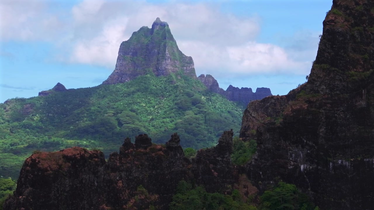 Picos vulcânicos altos e irregulares dramáticos de Moorea, terreno acidentado, Monte Rotui, Monte Toheia, Polinésia Francesa. Vista aérea de drone do Mirante Belvedere, Baía de Cook e Baía de Opunohu em uma manhã ensolarada com céu azul, nuvens e neblina baixa, com movimento de círculo à esquerda.
