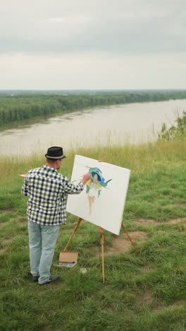 a painter in a hat, checkered shirt, and jeans, is focused on creating a masterpiece on a canvas in a grassy field beside a serene lake. a woman in a hat and white dress sits comfortably on a chair