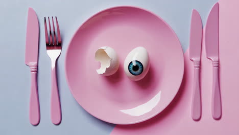 surreal eye in egg on pink plate with cutlery