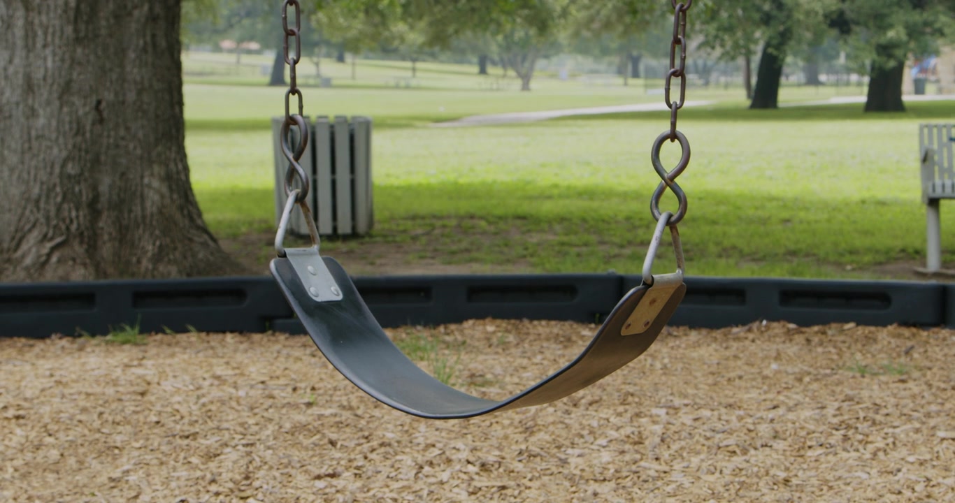 Eine einsame Schaukel schwingt sanft im Wind in einem leeren Stadtpark und ruft ein Gefühl von Ruhe und Einsamkeit hervor. Die Szene fängt die Stille und friedliche Atmosphäre des verlassenen Parks ein