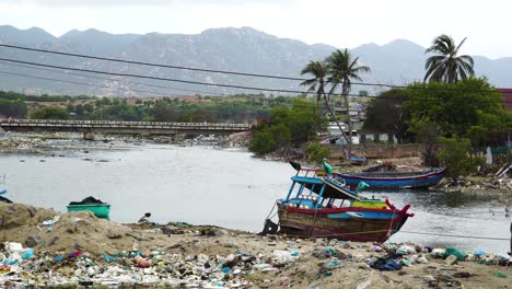 Leere-Boote,-Die-Auf-Einem-Mit-Müll-übersäten-Flussufer-Bei-Son-Hai-In-Vietnam-Ruhen