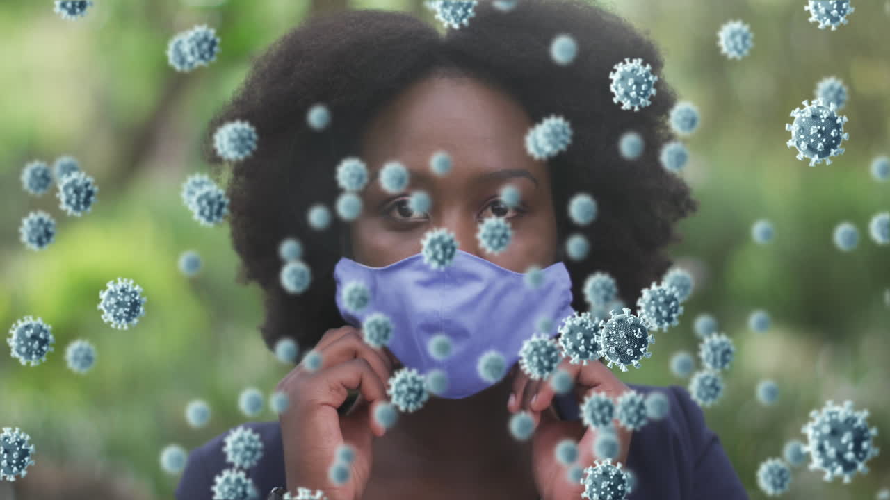 animación de células de coronavirus sobre una mujer afroamericana que se pone una máscara facial en el parque