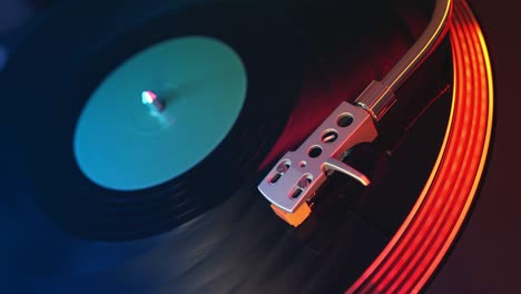 defocus in focus player vinyl records turntable closeup on a background of red and blue lights. the needle slides smoothly on a spinning black vinyl record