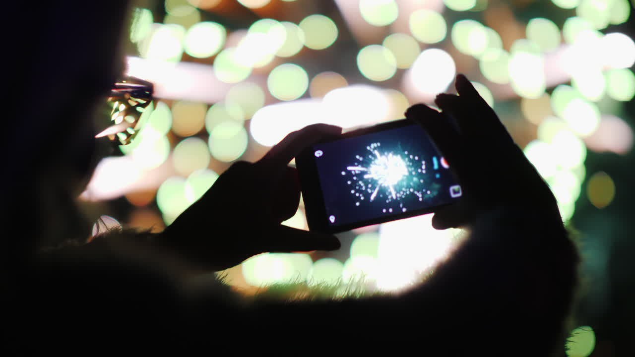 한 여성이 밤하늘의 불꽃놀이를 감상하고 스마트폰으로 사진을 찍습니다