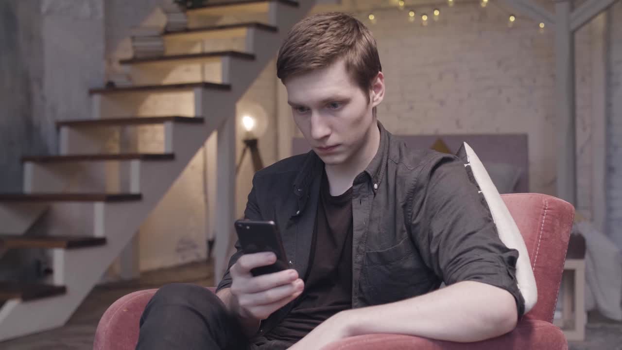 젊은 남자가 거실에서 전화로 문자 메시지를 보내고 있습니다.