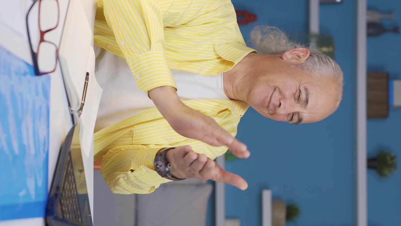 홈 오피스 직원의 수직 비디오 노인이 노트북에서 보는 것을 박수를 치고 있습니다.