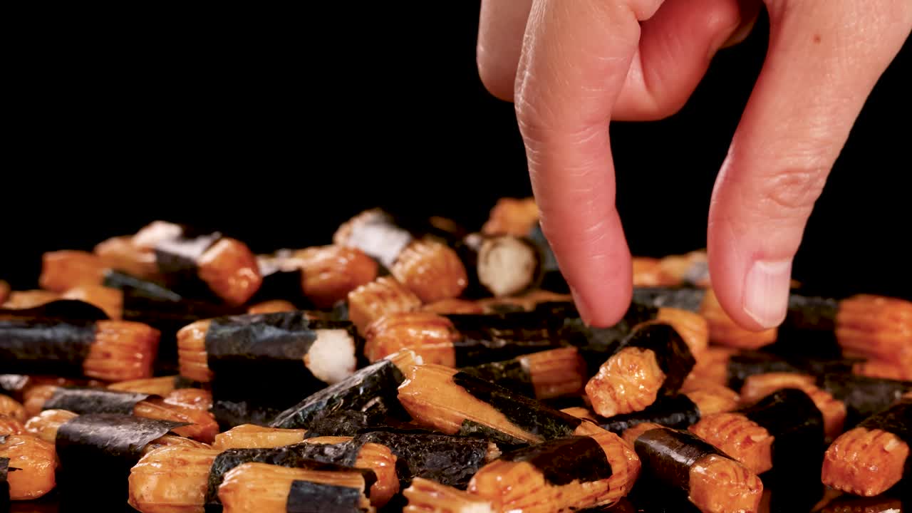 Human hand picks crunchy Japanese rice cracker from assorted snack pile, dramatic studio lighting